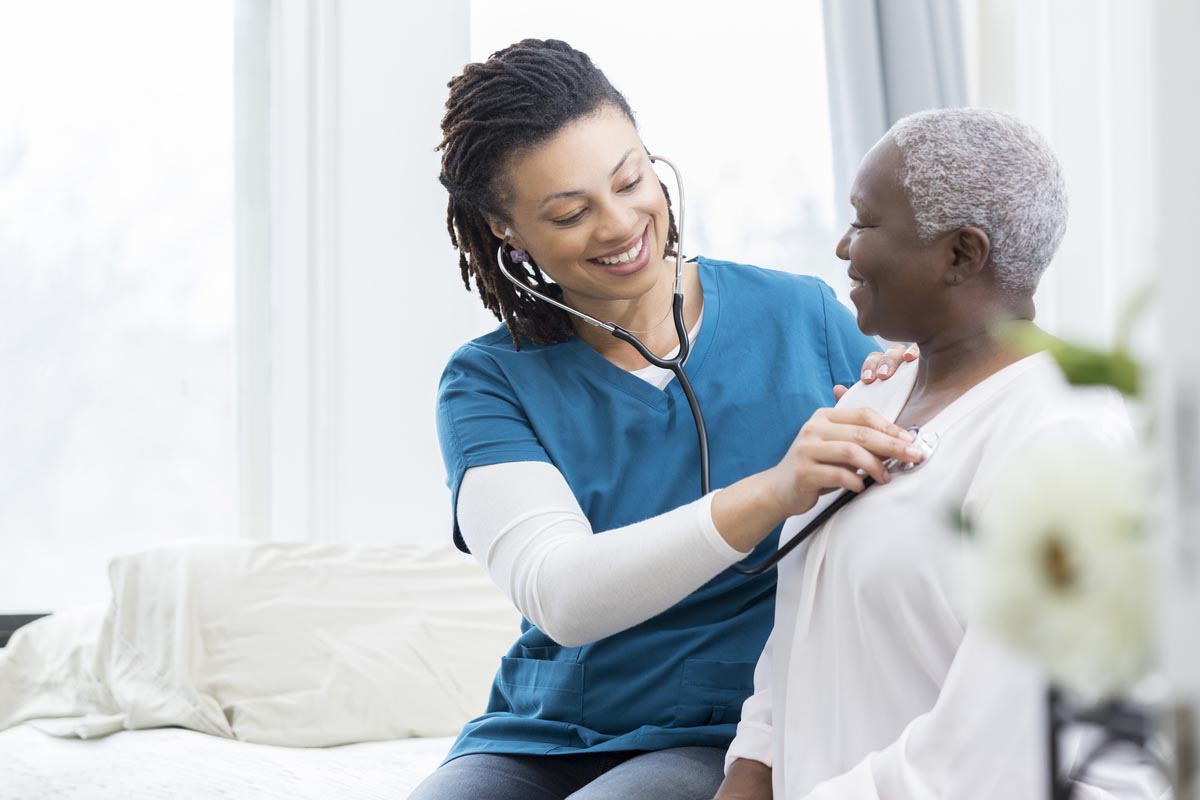 Young African American home healthcare nurse checks a senior female patient's vital signs. The senior woman is recovering at home from a recent surgery.